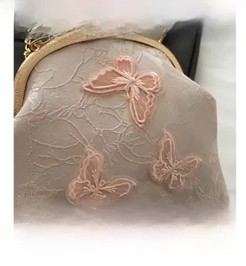 Detailed view of pink satin handbag featuring lace butterfly embroidery and gold clasp