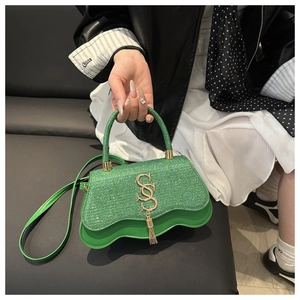 Détail du sac vert à paillettes avec franges logo S doré et bordure inférieure ondulée