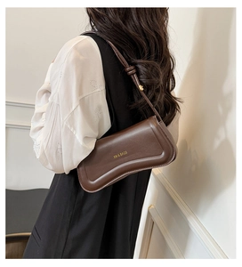 Model wearing a dark brown leather baguette bag with a gold logo and adjustable strap