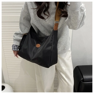 Detailed view of black nylon tote bag with brown leather accents shown on a model