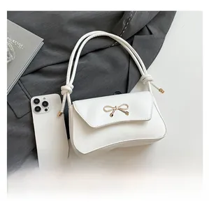 Detail of white PU shoulder bag featuring a gold bow clasp and decorative knotted straps