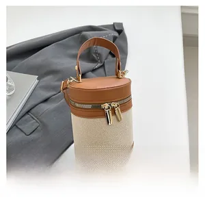 Detail view of cylinder bag featuring beige canvas and brown leather with gold zippers