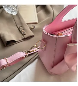 Detail of pink faux leather handbag showing golden metal hardware and large leather bow
