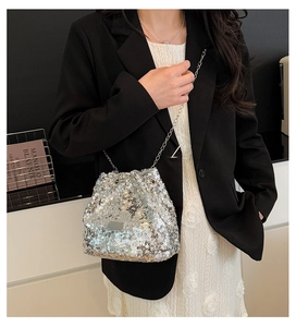 Detailed view of silver sequin bucket bag with metal chain strap worn by a model