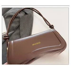 Detail of dark brown leather underarm bag with gold XM & BAGS logo lettering and fine stitching
