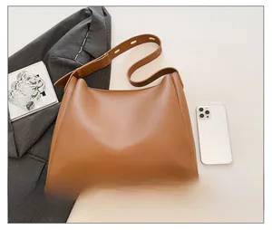 Top view of brown leather Hobo bag with adjustable strap next to a phone for size
