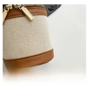 Close-up of off-white canvas bucket bag with brown leather trim and golden metal zipper