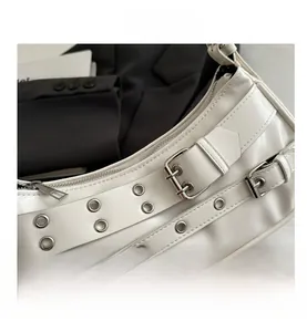 Detail of white Y2K style shoulder bag featuring silver grommets and buckle straps
