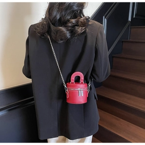 Close-up of red mini cylindrical bucket bag with silver chain strap on black blazer