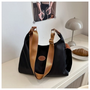 Detail of black nylon tote bag with brown woven strap and oval leather logo patch