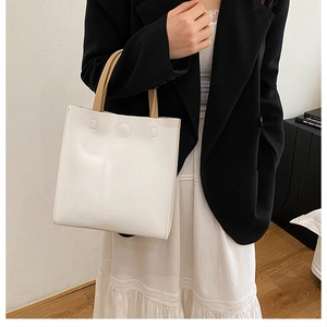 White minimalist square handbag with tan cylindrical handles on a business casual outfit