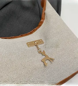 Close-up of beige woven canvas tote with brown leather trim and golden deer charm