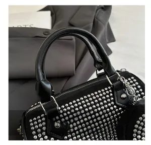 Close-up of black cylinder bag with silver studs, leather handle and metal zipper detail