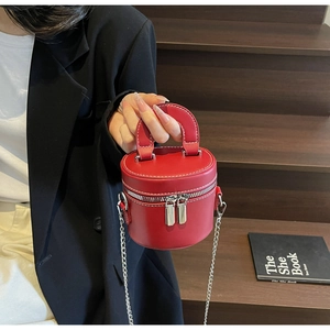 Detail of red cylindrical bucket bag with white stitching and double zipper design