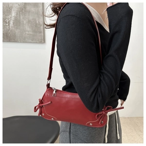 Detail shot of a dark red PU leather shoulder bag with side ribbon bows and silver rivets