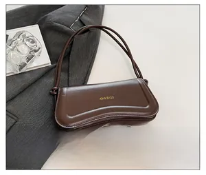 Detail view of a dark brown faux leather shoulder bag with gold logo and curved bottom