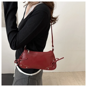 Detail view of red leather underarm bag featuring side bow ties and silver metallic studs