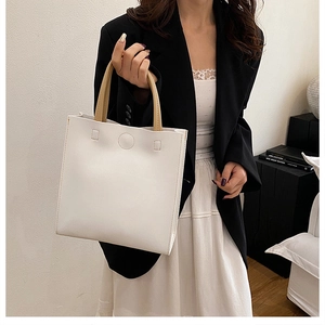 Close-up of a minimalist white leather handbag with contrast khaki handle held by a model
