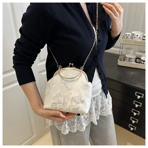 Macro detail of white lace shell bag featuring 3D butterfly appliques and metal handle