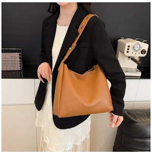 Detail of a brown leather tote bag with adjustable shoulder strap on a model
