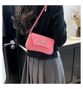 Detail of a pink leather shoulder bag featuring a golden bow buckle and slim strap