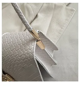Detailed close-up of gold metal link hardware on a white crocodile pattern handbag