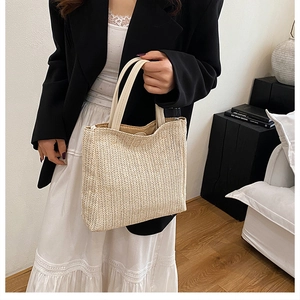 Detail of handwoven straw tote bag with cream leather handles held by a model