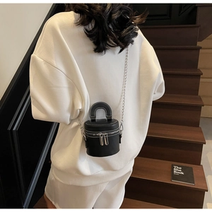 Detail of black cylindrical bucket bag with white contrast stitching and dual zippers