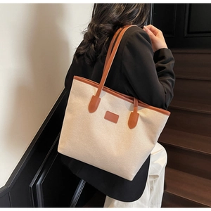 Detailed view of a large canvas tote bag with brown leather trim worn on the shoulder