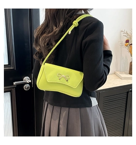 Detail of neon green shoulder bag featuring a golden metal bow and elegant knotted strap