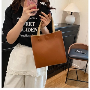 Detail of minimalist brown tote bag with light beige handles shown in a lifestyle mirror shot
