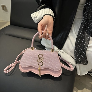 Sac à bandoulière rose à paillettes avec détails dorés et pompon sur canapé noir