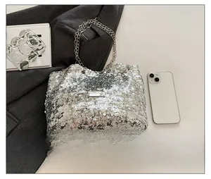 Detail of silver sequin tote bag with dual chain straps next to a smartphone for scale