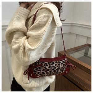 Detail view of leopard print shoulder bag with red trim and bow tie accents on model