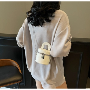 White mini bucket bag with silver chain strap shown on model in a modern interior