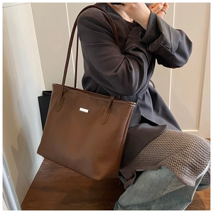 Detailed view of brown lychee leather tote bag with silver metal plate and thin straps