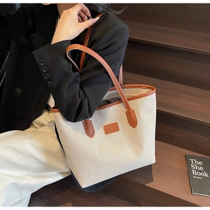 Model wearing large canvas tote bag with brown leather trim on wooden stairs