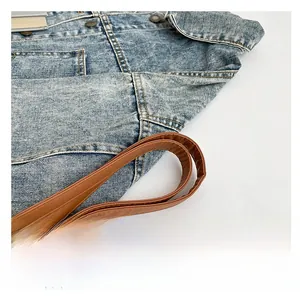 Detail of blue denim tote bag featuring brown faux leather handles and metal rivets