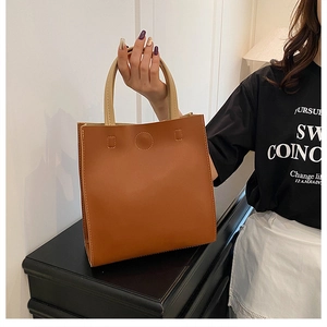 Detailed view of brown leather tote bag with contrast stitching and embossed round detail