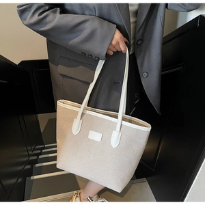 Detail of a large canvas tote bag with contrast leather straps worn over a grey blazer