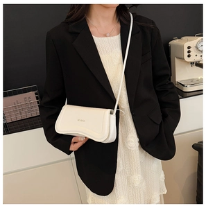 Model showing a cream white leather flap crossbody bag with brand logo on a black blazer