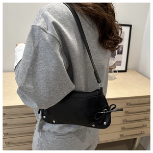 Side view of black faux leather underarm bag with double bow details and silver rivets