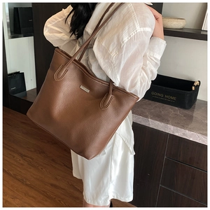 Gros plan sur un sac cabas marron en cuir grainé avec logo métallique porté par un mannequin