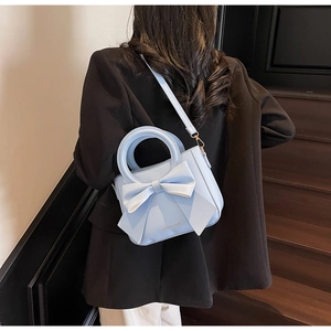 Light blue bucket bag with bow detail worn over a black blazer in a modern setting