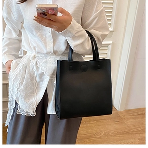 Detail of minimalist black tote bag featuring round handles and smooth matte faux leather texture