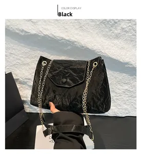 Detail der schwarzen Plissee-Tasche mit goldener Metallkette und rundem Schnallenverschluss