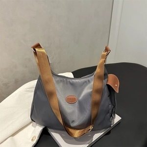 Minimalist grey nylon half-moon tote bag with brown wide strap and fashion leather patch