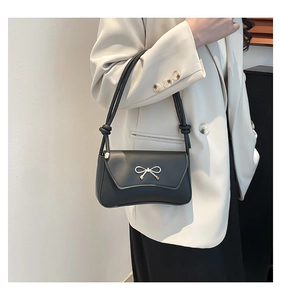 Detail of black leather underarm bag with gold bow ornament and knotted shoulder strap