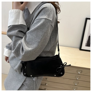 Detail of black glossy shoulder bag featuring silver rivets and side bow decorations