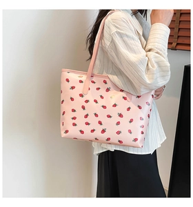 Detail of pink strawberry print tote bag shown on shoulder with glossy leather finish